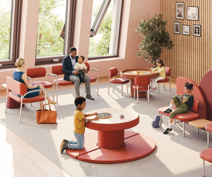 Coradle by MooreCo pediatric healthcare waiting room with adult and children's seating, sensory activity table, and room divider in warm terracotta tones